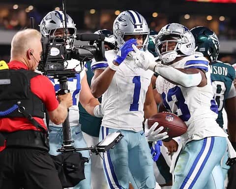 Celebrating a touchdown at an NFL game, Dallas Cowboys players cheer as a teammate scores, with a cameraman capturing the victorious moment during the football game.