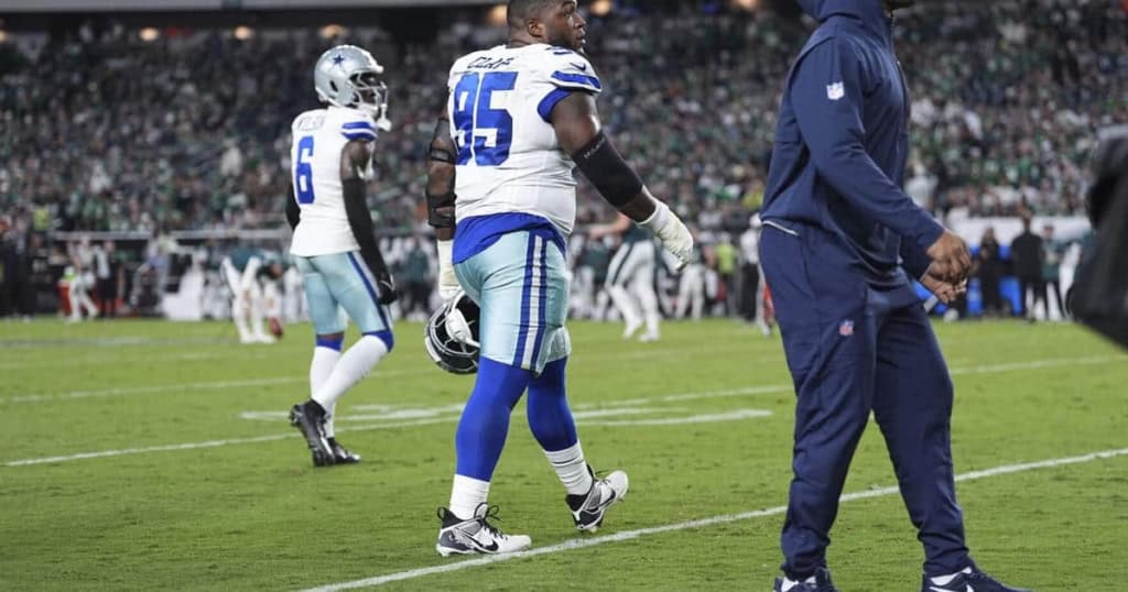 Dallas Cowboys football players on the field during a game at AT&T Stadium, showcasing team uniforms, coaching staff, and game action. The stadium is packed with fans enjoying the NFL match.