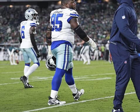Dallas Cowboys football players on the field during a game at AT&T Stadium, showcasing team uniforms, coaching staff, and game action. The stadium is packed with fans enjoying the NFL match.