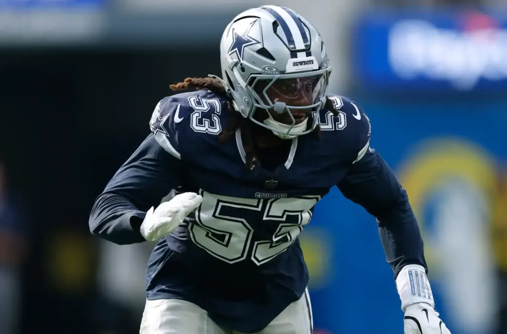 Dallas Cowboys player in action during a game, wearing helmet and dark jersey, focused on the play, symbolizing NFL sportsmanship and athleticism.