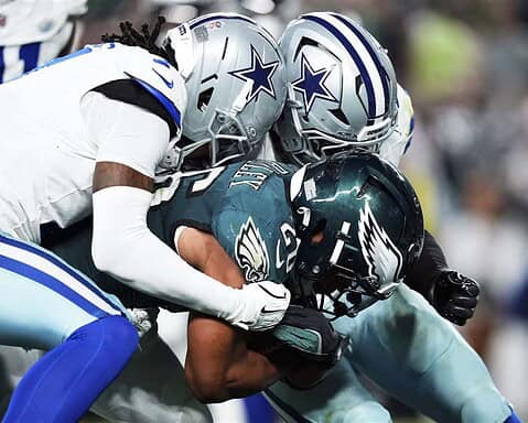 Aggressive tackle during an NFL game between Dallas Cowboys and Philadelphia Eagles, showcasing intense football action, player helmets, and team uniforms.