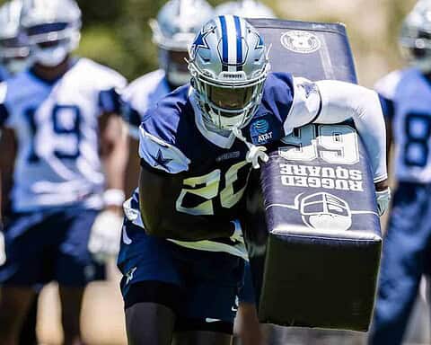 Dallas Cowboys football player practicing during training camp with teammates on the field.