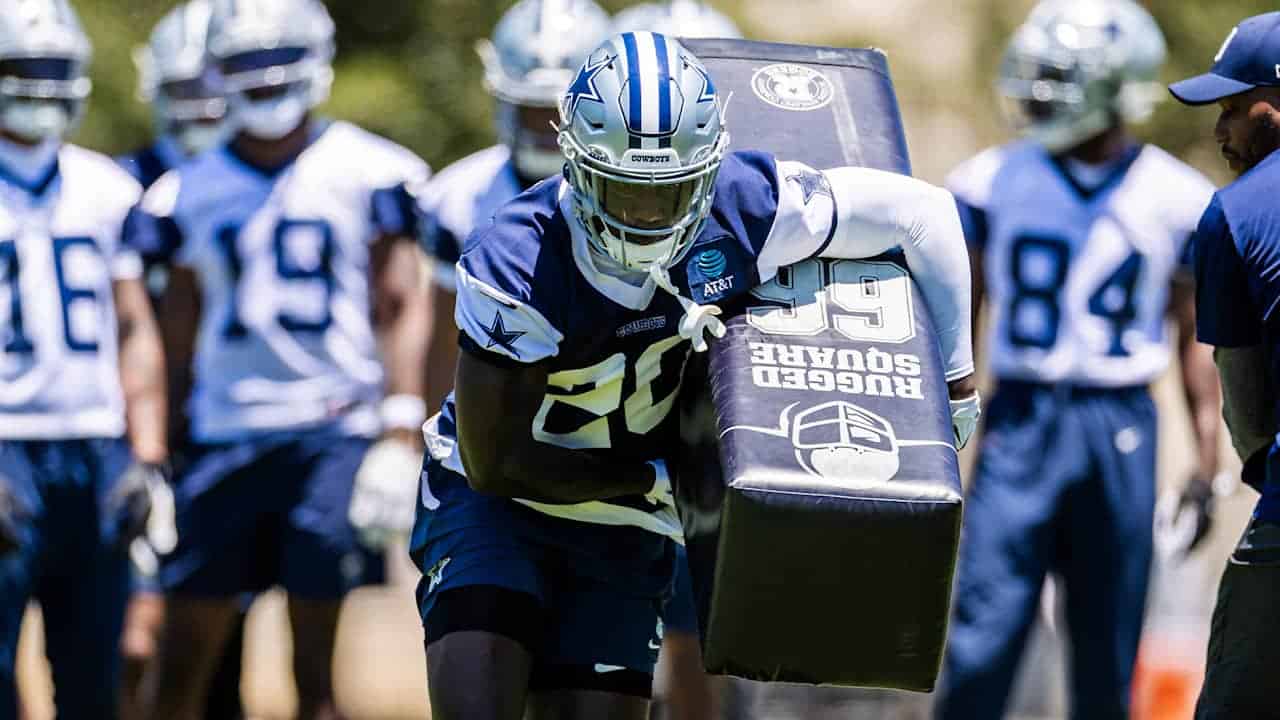 Dallas Cowboys football player practicing during training camp with teammates on the field.