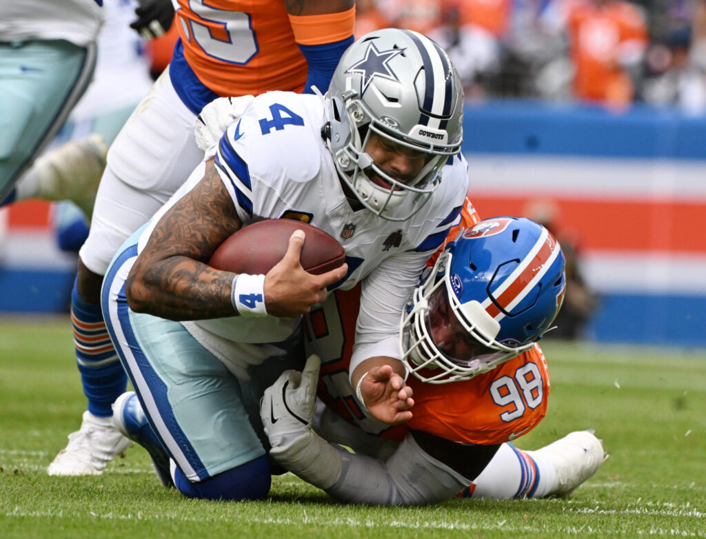 Running back holding football being tackled by defensive players during an NFL game, showcasing intense action and player athleticism from Dallas Cowboys and Denver Broncos.