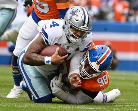 Running back holding football being tackled by defensive players during an NFL game, showcasing intense action and player athleticism from Dallas Cowboys and Denver Broncos.