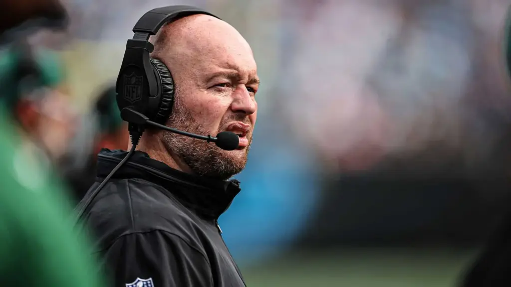 Head coach wearing NFL headset during football game, focused on sidelines, close-up shot.