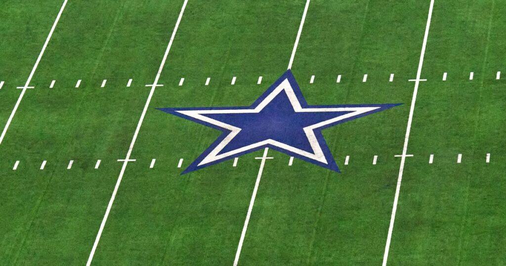Dallas Cowboys star logo on the football field, representing the NFL team, inside AT&T Stadium, with bright green turf and white yard lines.