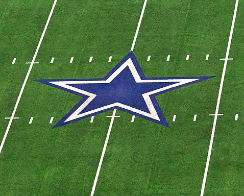 Dallas Cowboys star logo on the football field, representing the NFL team, inside AT&T Stadium, with bright green turf and white yard lines.