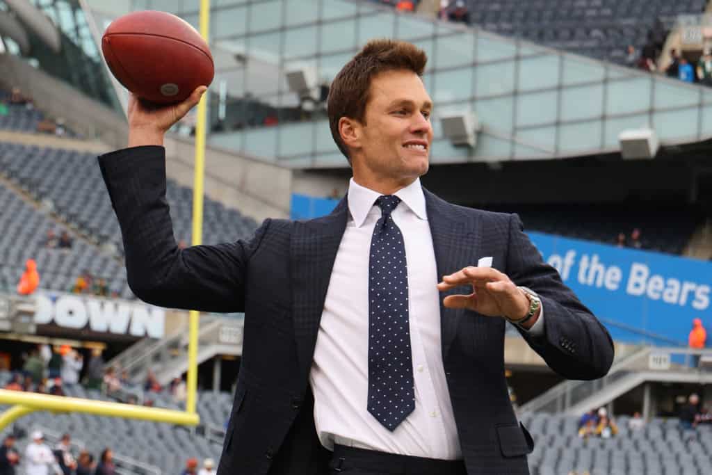 Quarterback throwing a football at AT&T Stadium during a Dallas Cowboys game, dressed in formal suit and tie, highlighting NFL sports and football stadium atmosphere.