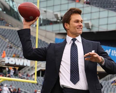Quarterback throwing a football at AT&T Stadium during a Dallas Cowboys game, dressed in formal suit and tie, highlighting NFL sports and football stadium atmosphere.