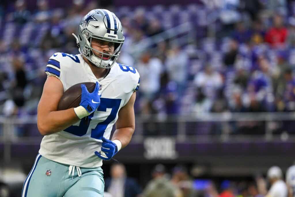 Running back player from the Dallas Cowboys holding a football during a game, wearing a silver helmet with Dallas star logo, in a crowded stadium with fans, showcasing NFL football action.