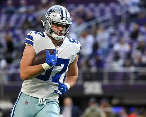 Running back player from the Dallas Cowboys holding a football during a game, wearing a silver helmet with Dallas star logo, in a crowded stadium with fans, showcasing NFL football action.