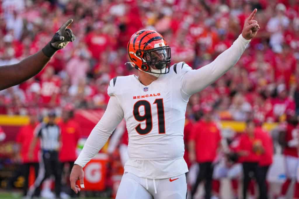 Cincinnati Bengals player celebrating on the football field during a game, wearing a white uniform with the number 91, with a crowd in the background.