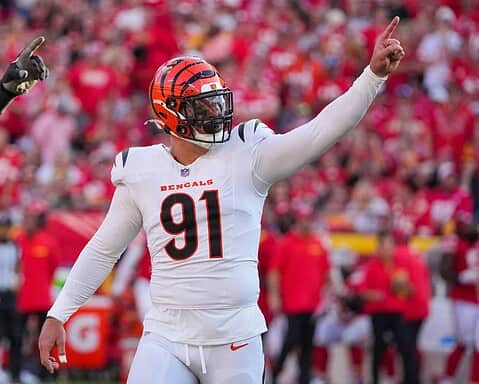 Cincinnati Bengals player celebrating on the football field during a game, wearing a white uniform with the number 91, with a crowd in the background.