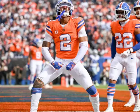 Celebrating a touchdown on the field, Denver Broncos players in their orange and white uniforms during an NFL game. The crowd cheers loudly in the background at Empower Field at Mile High.