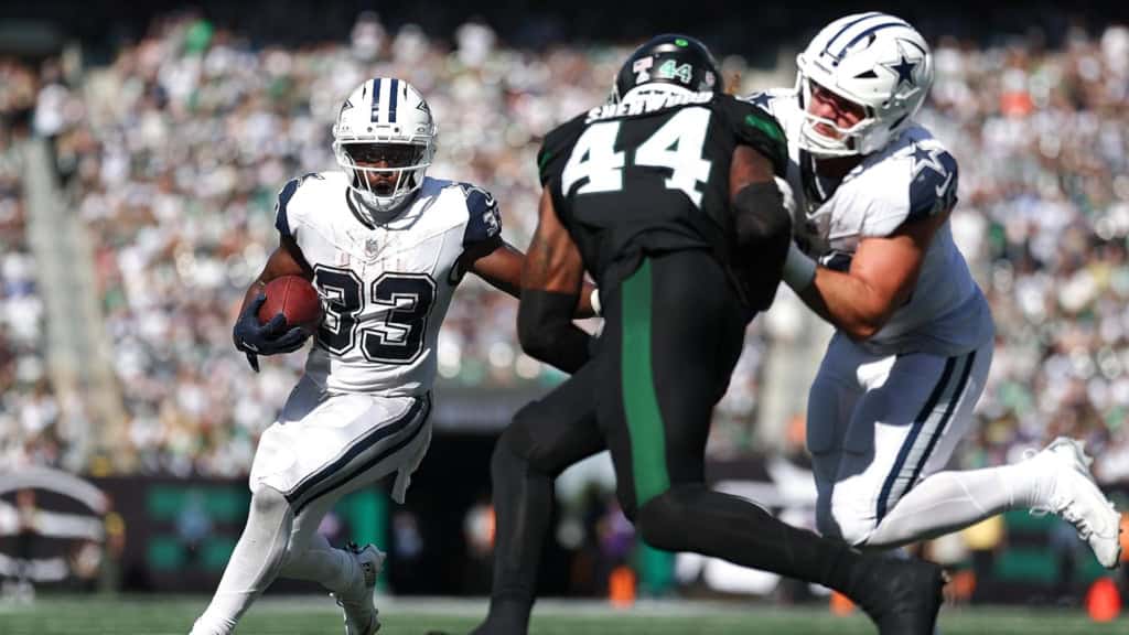 Running back with the football evades two defenders during an National Football League game, showcasing the Dallas Cowboys' offensive play against the opposing team.