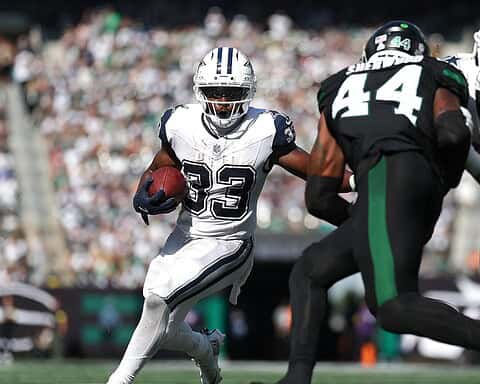 Running back with the football evades two defenders during an National Football League game, showcasing the Dallas Cowboys' offensive play against the opposing team.