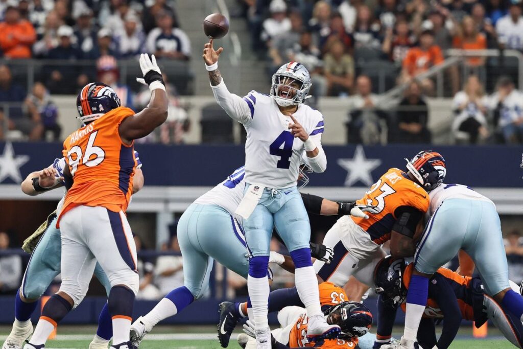Quarterback throws football during NFL game between Dallas Cowboys and Denver Broncos, with defensive players trying to block the pass, action shot of American football game in stadium.