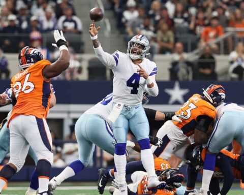 Quarterback throws football during NFL game between Dallas Cowboys and Denver Broncos, with defensive players trying to block the pass, action shot of American football game in stadium.