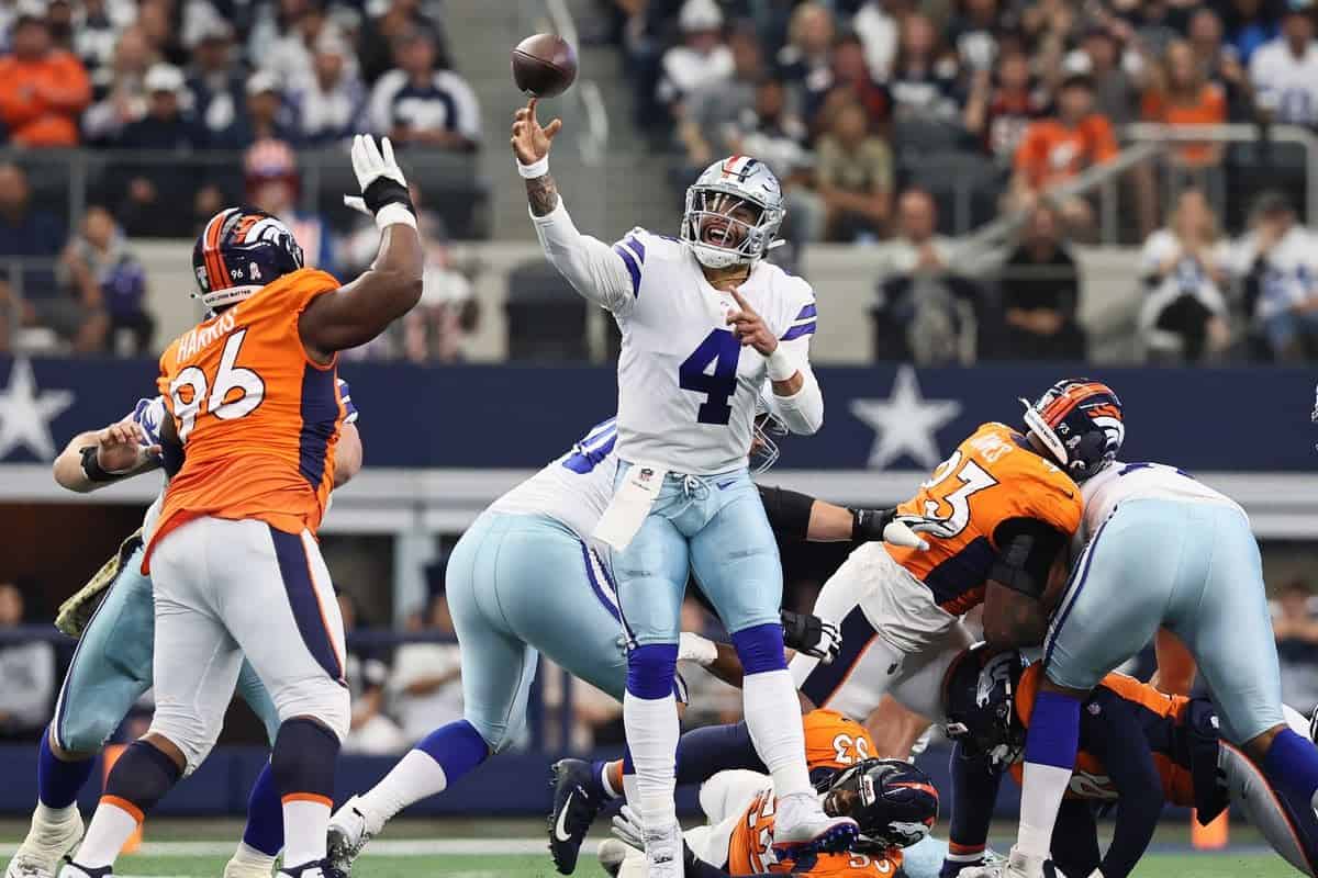 Quarterback throws football during NFL game between Dallas Cowboys and Denver Broncos, with defensive players trying to block the pass, action shot of American football game in stadium.