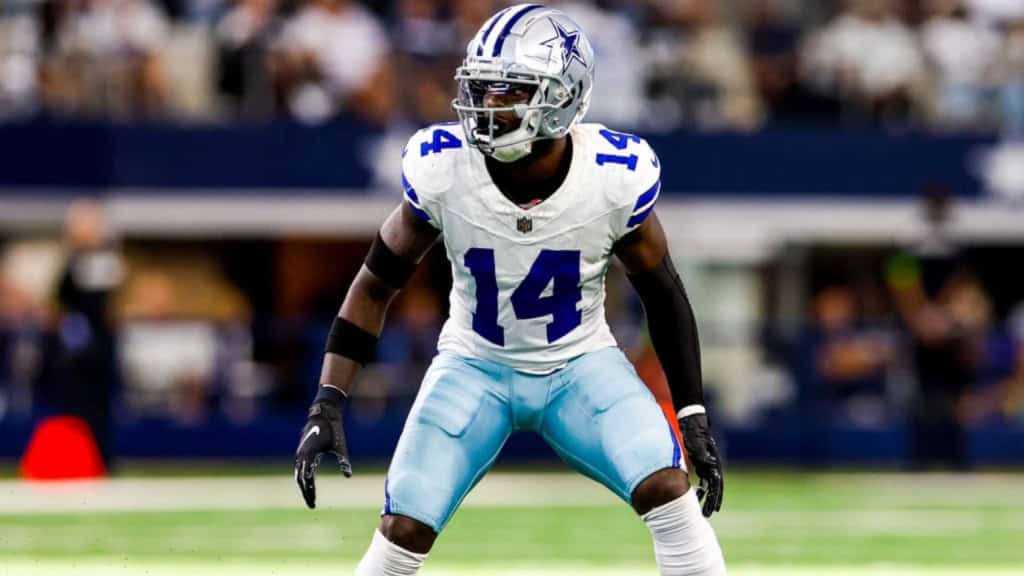 Joueur de football américain des Dallas Cowboys en position de défense sur le terrain, portant un uniforme blanc et bleu avec le numéro 14, lors d'un match de NFL.