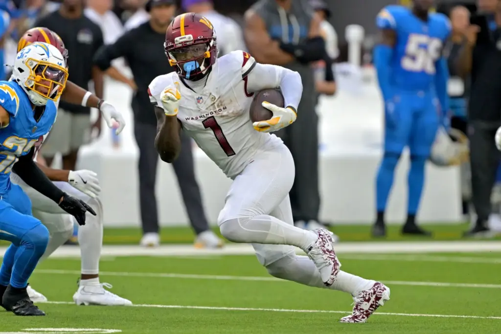 D.C. Football player running with the ball during an NFL game, wearing a white uniform with number 1, on the field with opponents in blue uniforms, crowd in the background.