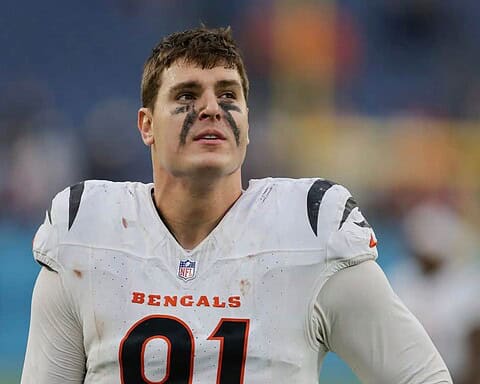 Young football player in Cincinnati Bengals uniform with black face paint, on the field during a game. Focused and determined, showcasing sports passion and NFL team spirit.