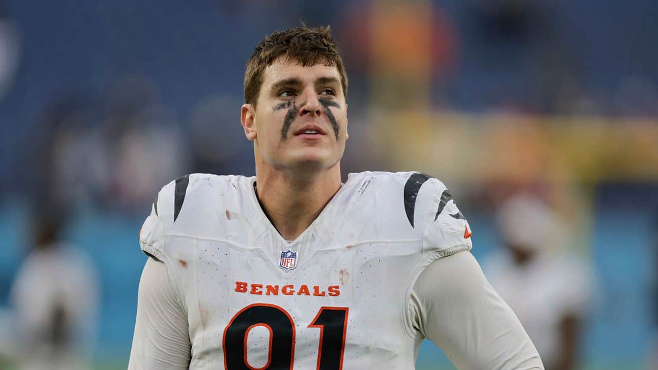 Young football player in Cincinnati Bengals uniform with black face paint, on the field during a game. Focused and determined, showcasing sports passion and NFL team spirit.