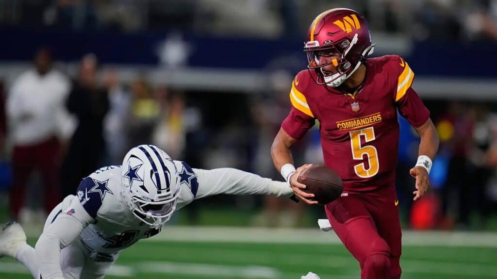 Quarterback in Washington Commanders uniform evading defender from Dallas Cowboys during an NFL game.