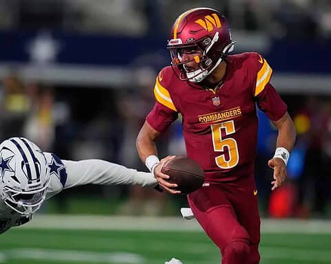 Quarterback in Washington Commanders uniform evading defender from Dallas Cowboys during an NFL game.