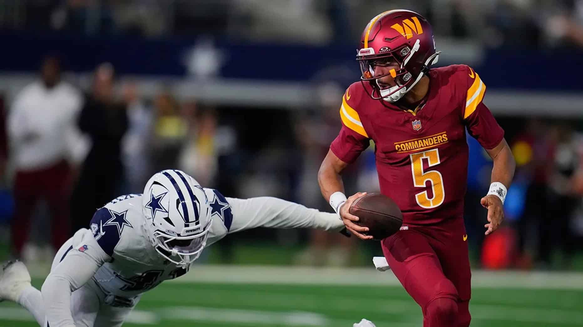 Quarterback in Washington Commanders uniform evading defender from Dallas Cowboys during an NFL game.