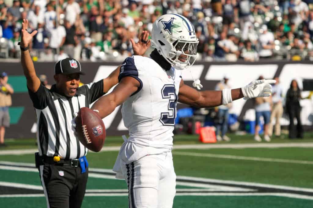 Dallas Cowboys football player celebrating after a touchdown, holding the football with an official behind him on the field during an NFL game.