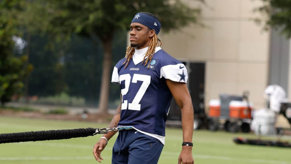 Dallas Cowboys football player during practice, wearing team jersey and headband, holding resistance band on green field.