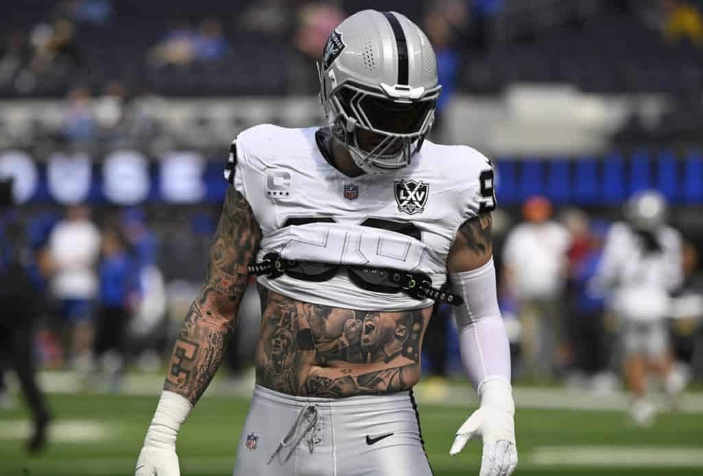 A professional football player wearing the Las Vegas Raiders uniform with tattoos on his torso and arms, celebrating during an NFL game on the field.