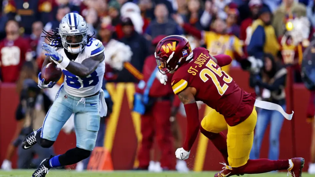 Exploring an intense football game between Dallas Cowboys and Washington Football Team, featuring a Cowboy running with the ball as a Washington defender attempts to tackle him on the field.