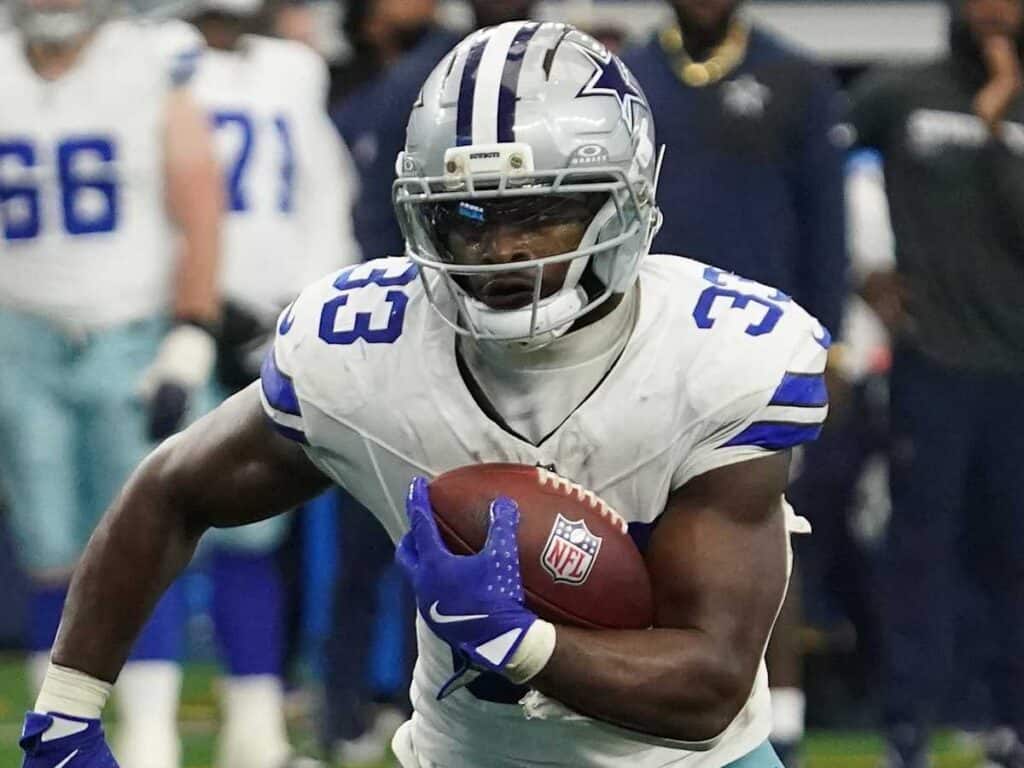 Fast football player running with ball, wearing Dallas Cowboys uniform, in game action, on NFL field, focused and intense, showcasing American football athlete skills.