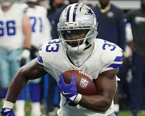 Fast football player running with ball, wearing Dallas Cowboys uniform, in game action, on NFL field, focused and intense, showcasing American football athlete skills.