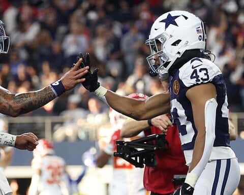 High-quality image of Dallas Cowboys players in football gear exchanging high-fives during a game, showcasing team spirit and on-field action.