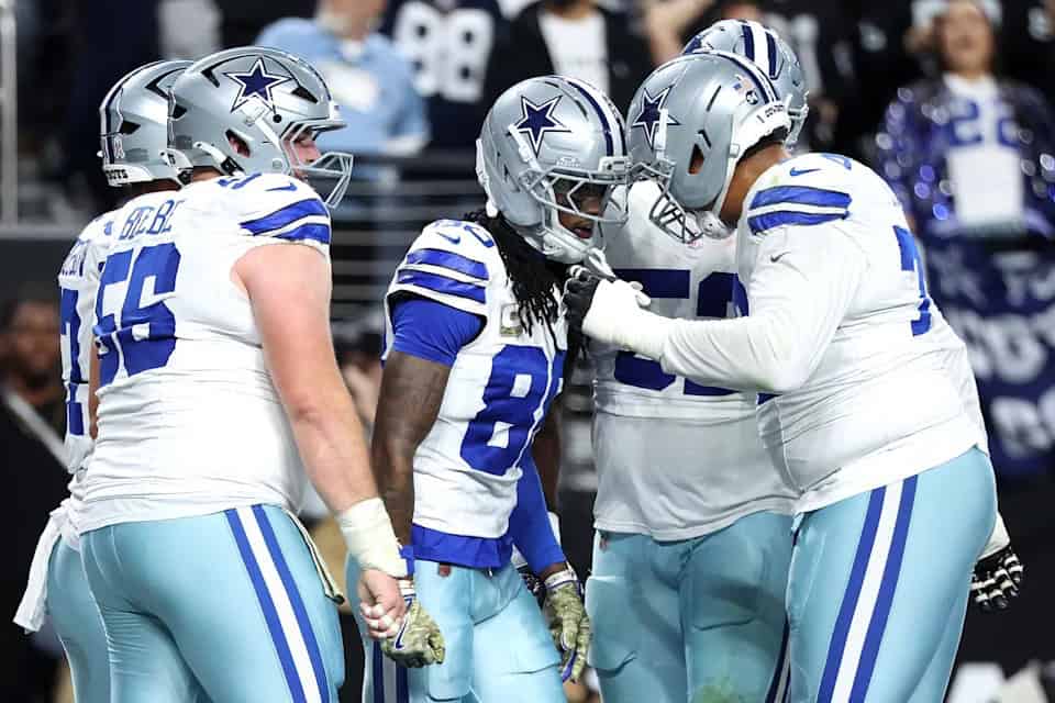 Dallas Cowboys football team celebrating during a game, wearing white and blue uniforms, with focus on team camaraderie and player unity, in a packed stadium.
