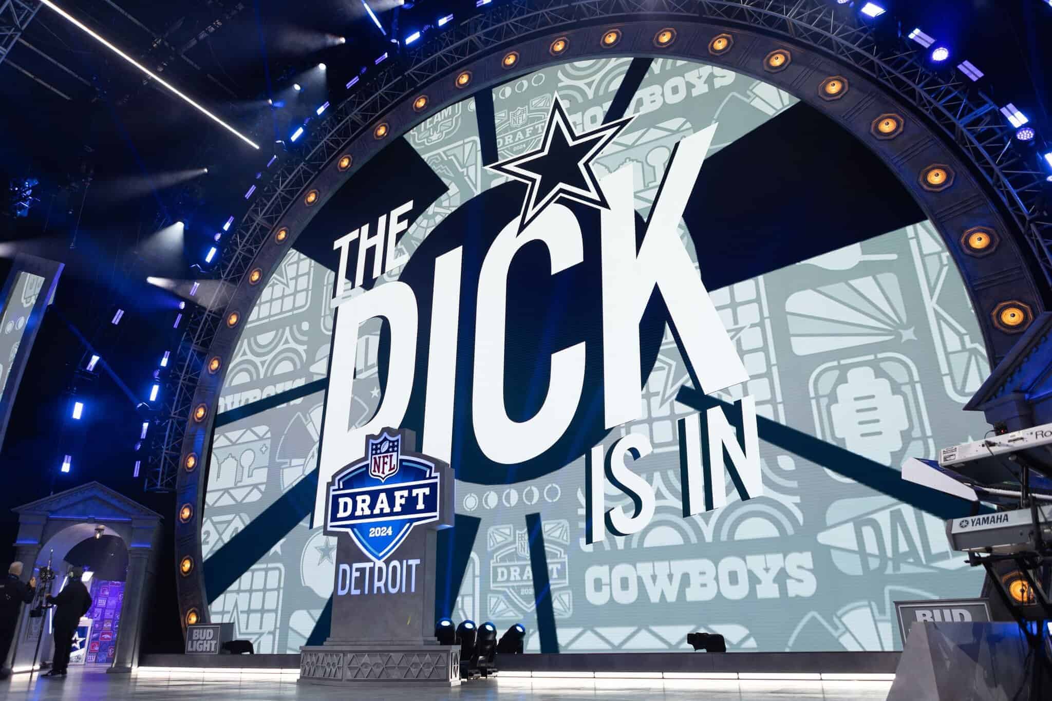 Draft NFL 2024 NFL Draft event stage with prominent Dallas Cowboys branding, large digital screen displaying "The Pick is In," surrounded by professional lighting and event setup.