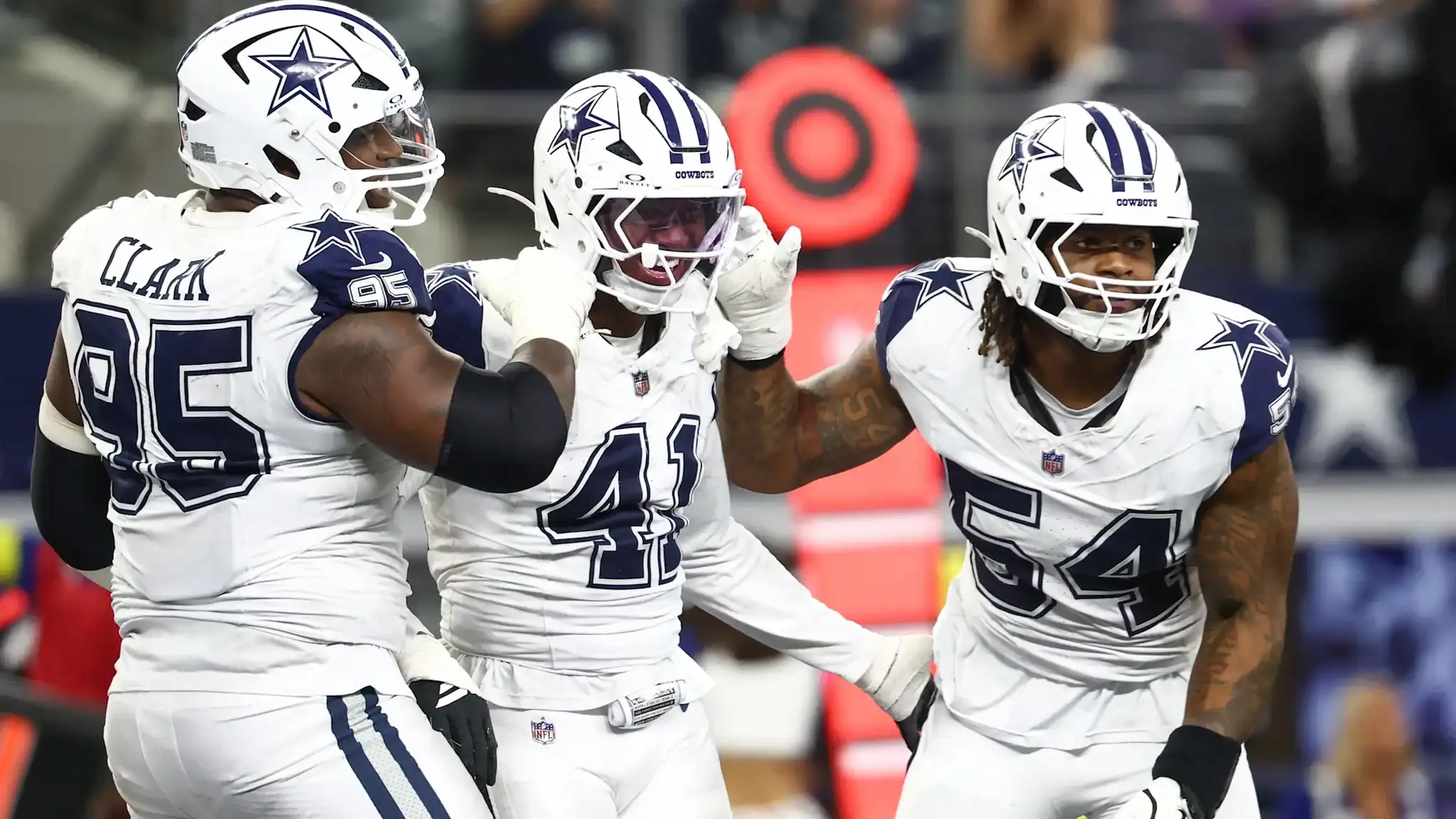 Celebrating Dallas Cowboys football players on the field wearing white jerseys and helmets with star logos, showcasing team camaraderie, during an NFL game.