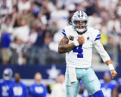 Dallas Cowboys football player celebrating on the field during an NFL game, wearing uniform with number 4, helmet, and tactical gear, emphasizing team spirit and game excitement.